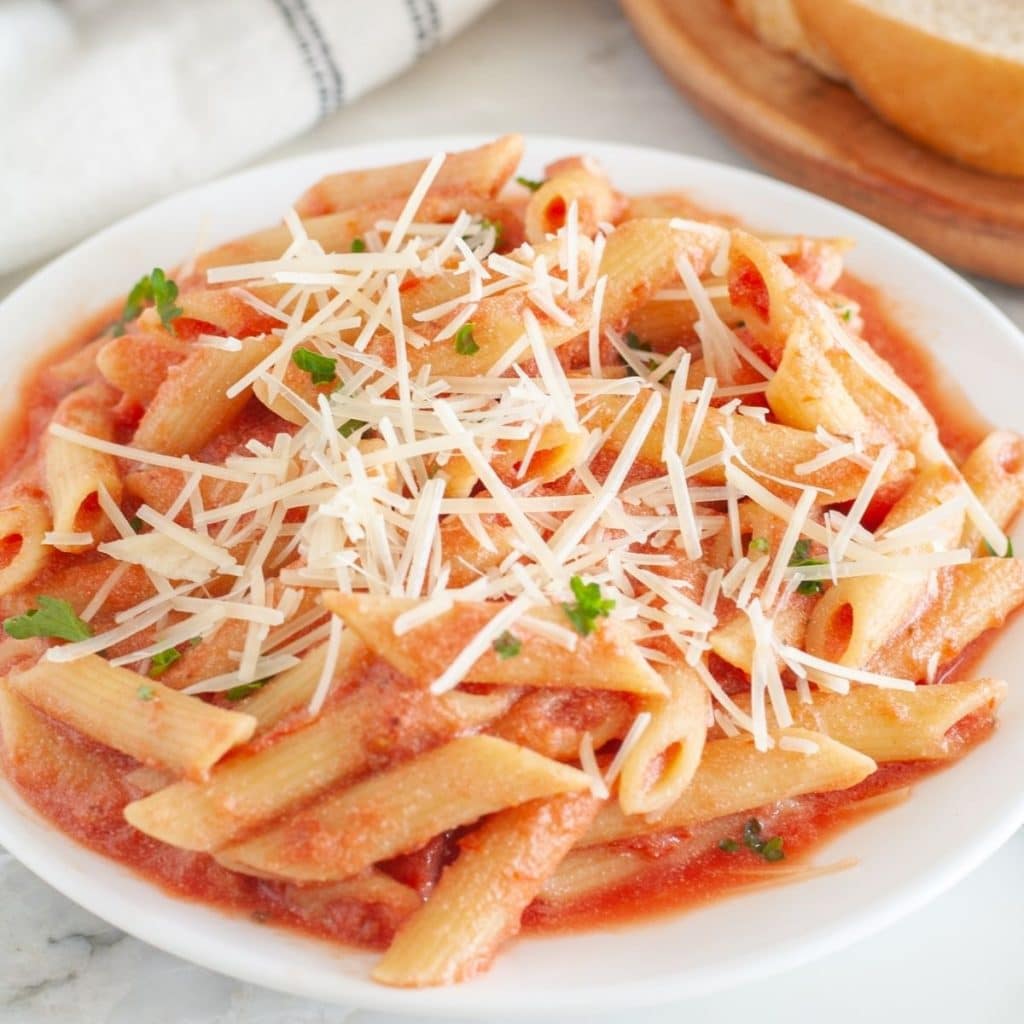 Plate of penne pasta with pink sauce and parmesan cheese.