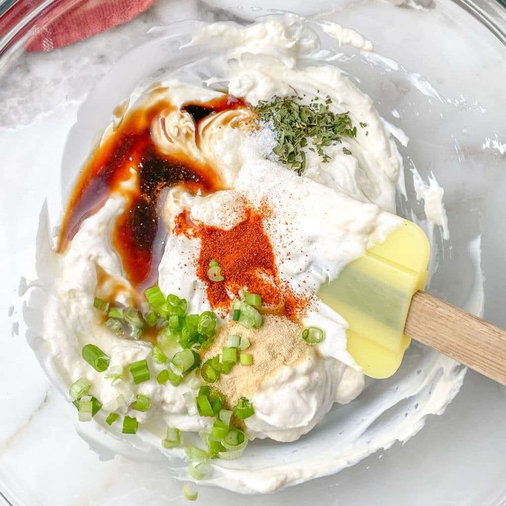 Bowl with spatula, sour cream, diced green onion, and seasonings.