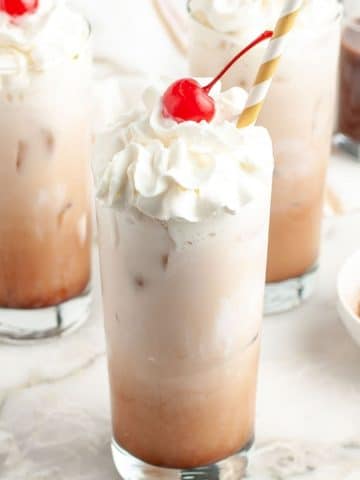Tall glass with creamy drink and a cherry on top.