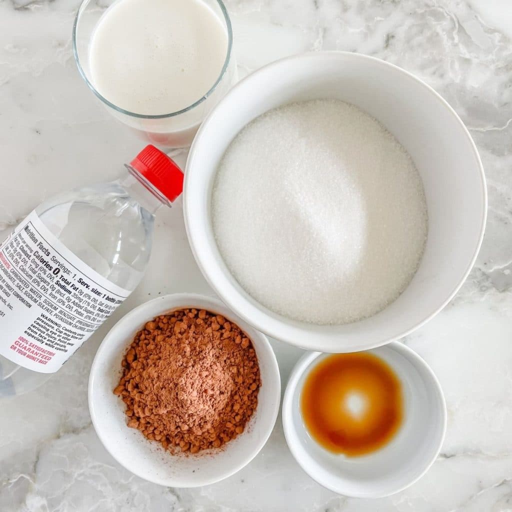 Bowl of sugar, bowl of cocoa powder, vanilla, milk, and soda water.