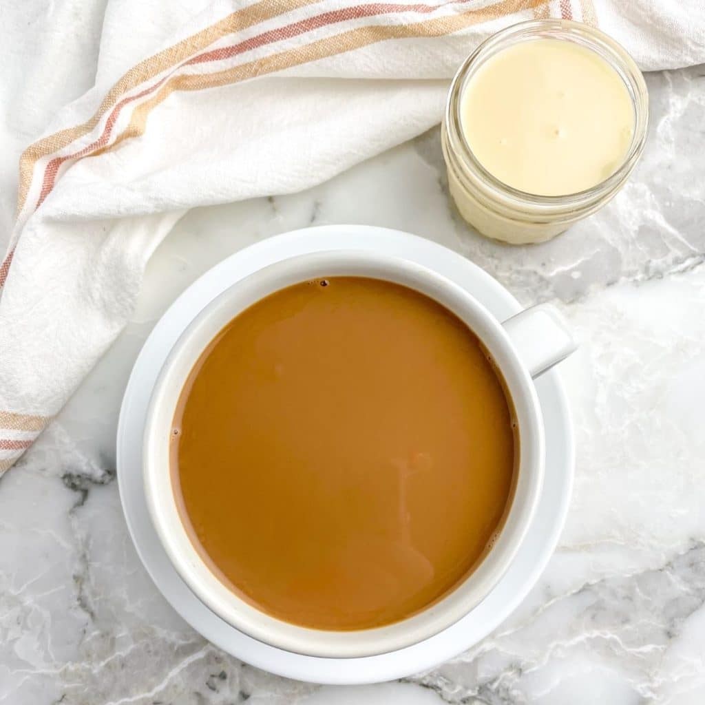 Looking down at a full cup of coffee and jar of condensed milk.