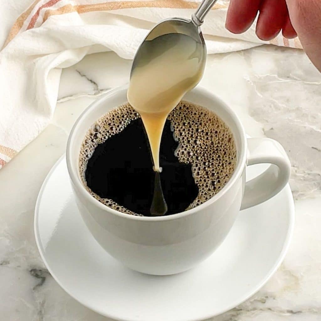 Spoon with condensed milk going into mug of coffee.