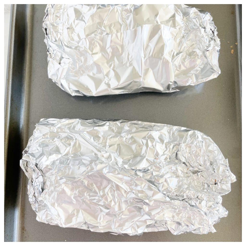 Ribs wrapped in foil on baking sheet.