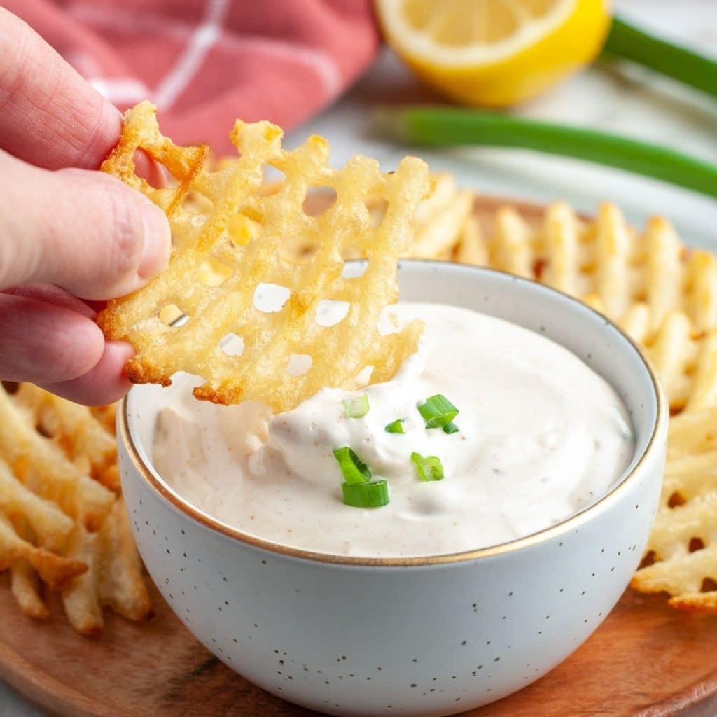 Waffle fry dipping into creamy sauce.