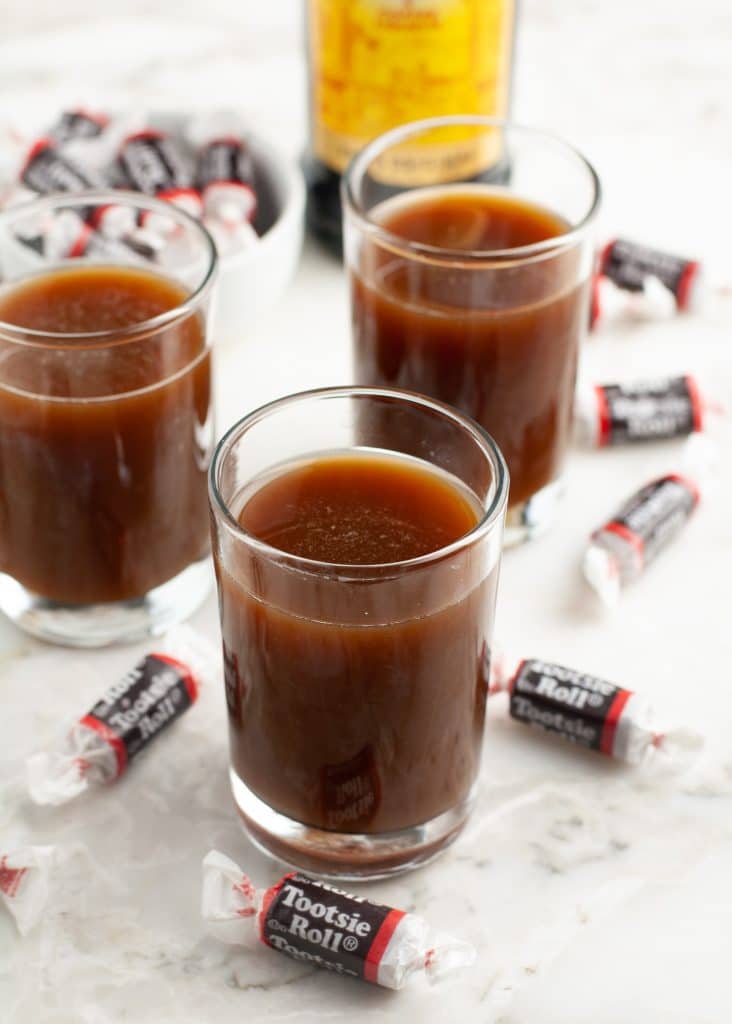 Three shot glasses full of dark drink and Tootsie roll candies. 