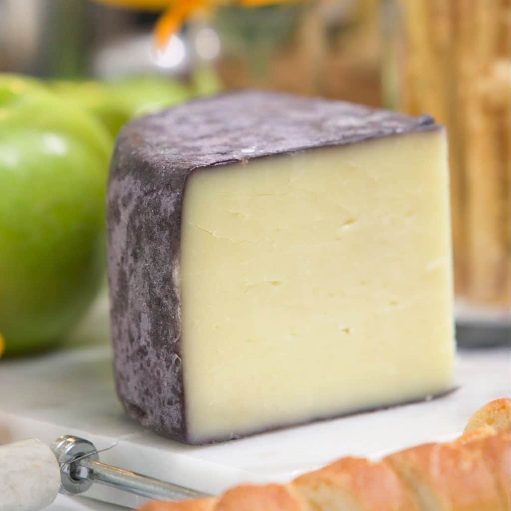 Wedge of cheese with dark rind on a cutting board.