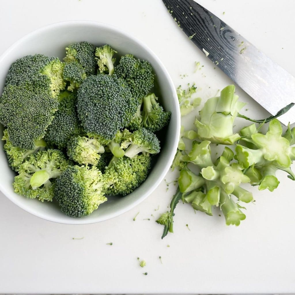 Broccoli florets in a bowl, broccoli stems and knife on cutting board.