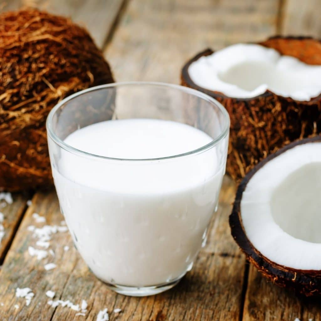 Glass of coconut milk and halved coconut.