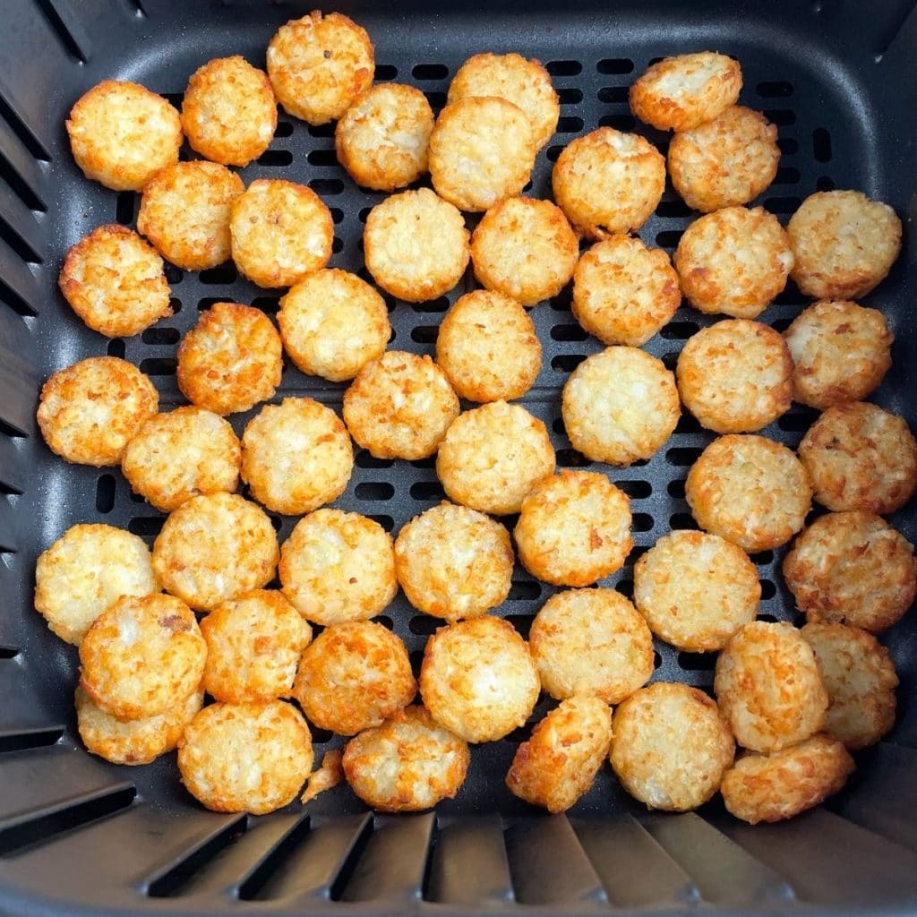 Cooked tater tots in air fryer basket.