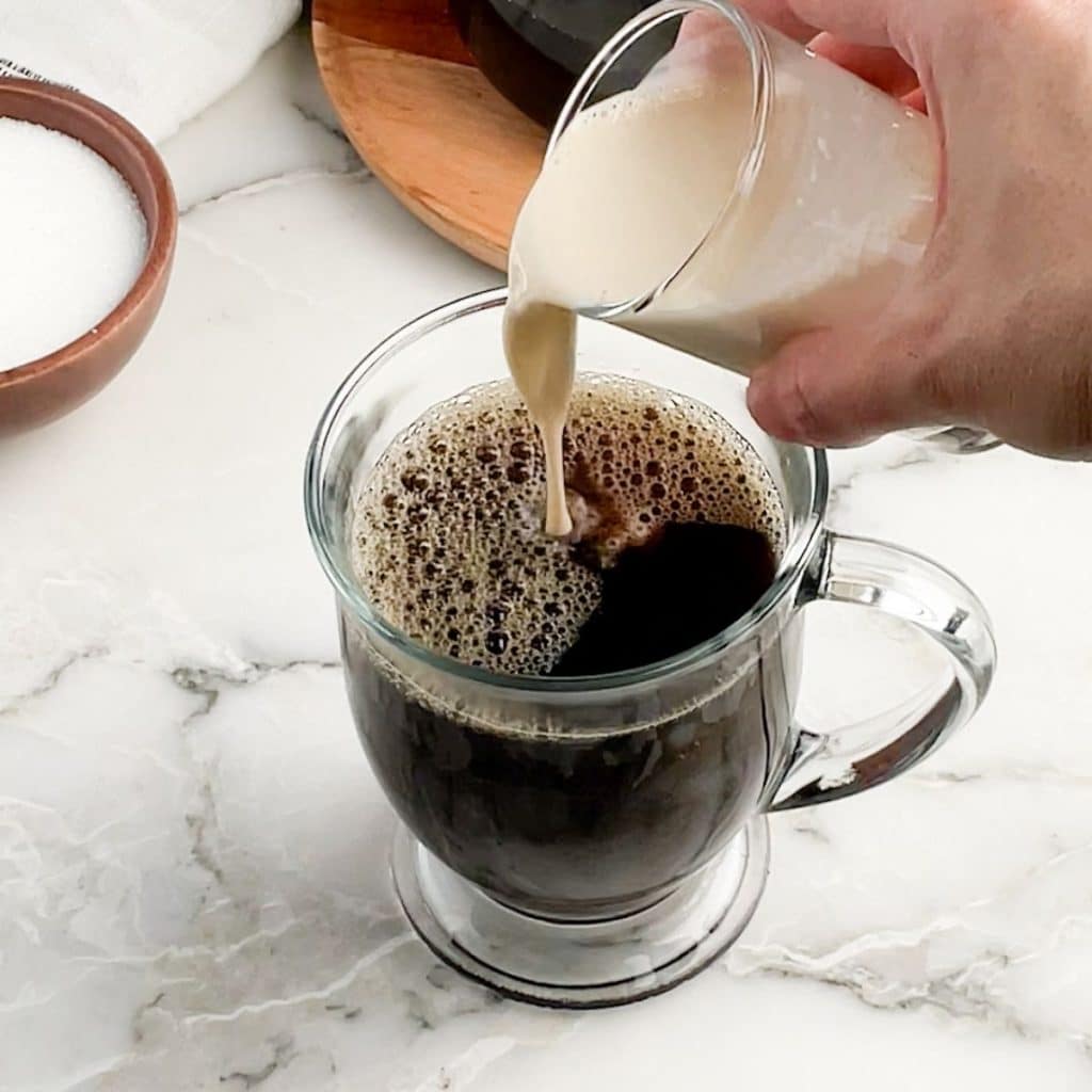 Milk pouring into mug of coffee.