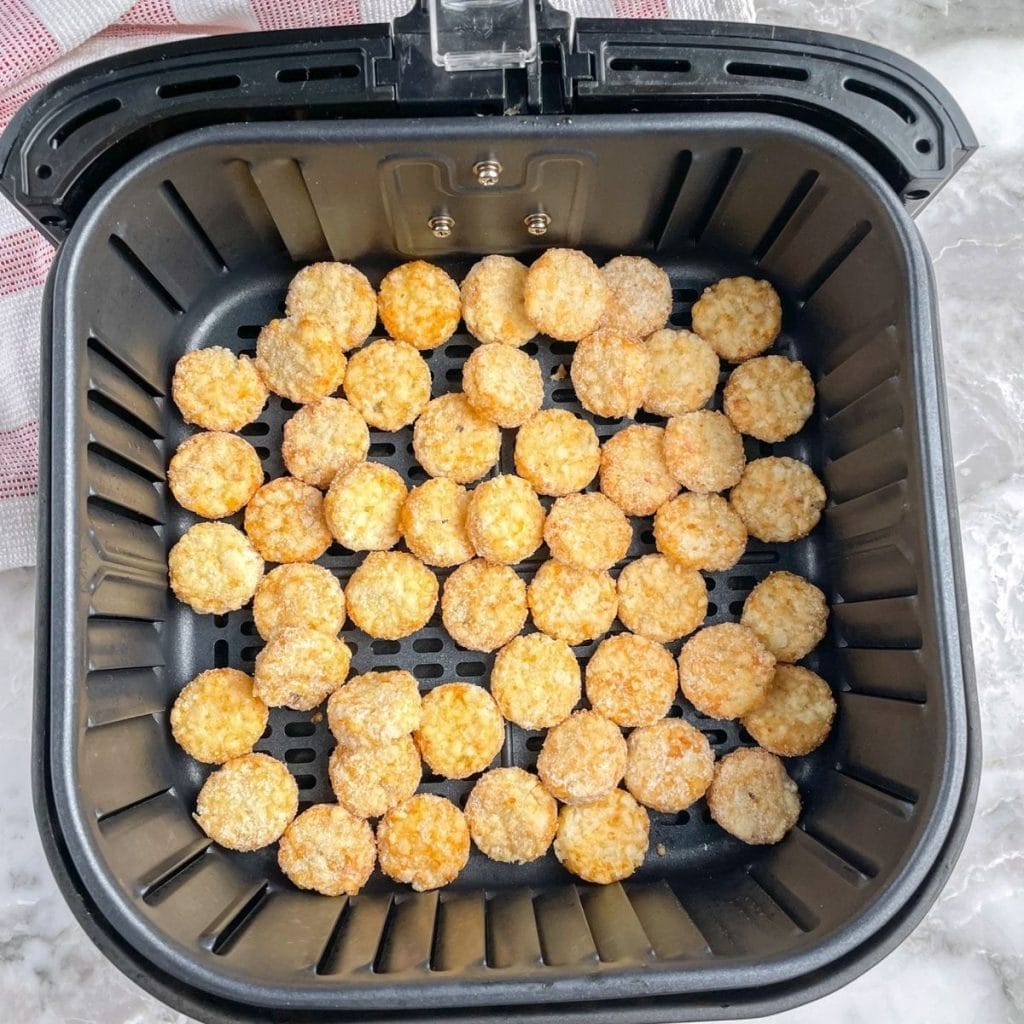 Frozen tater tots in air fryer basket.