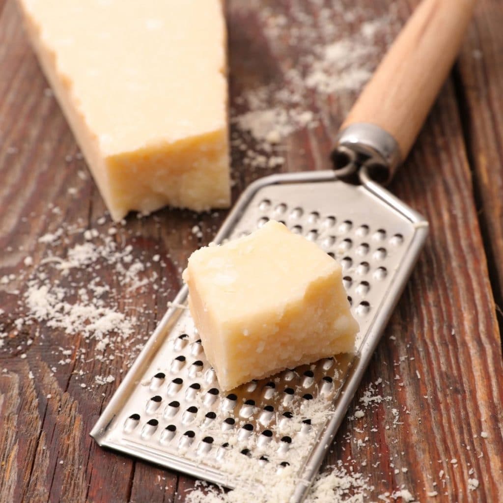 Grater with block of Parmesan cheese. 
