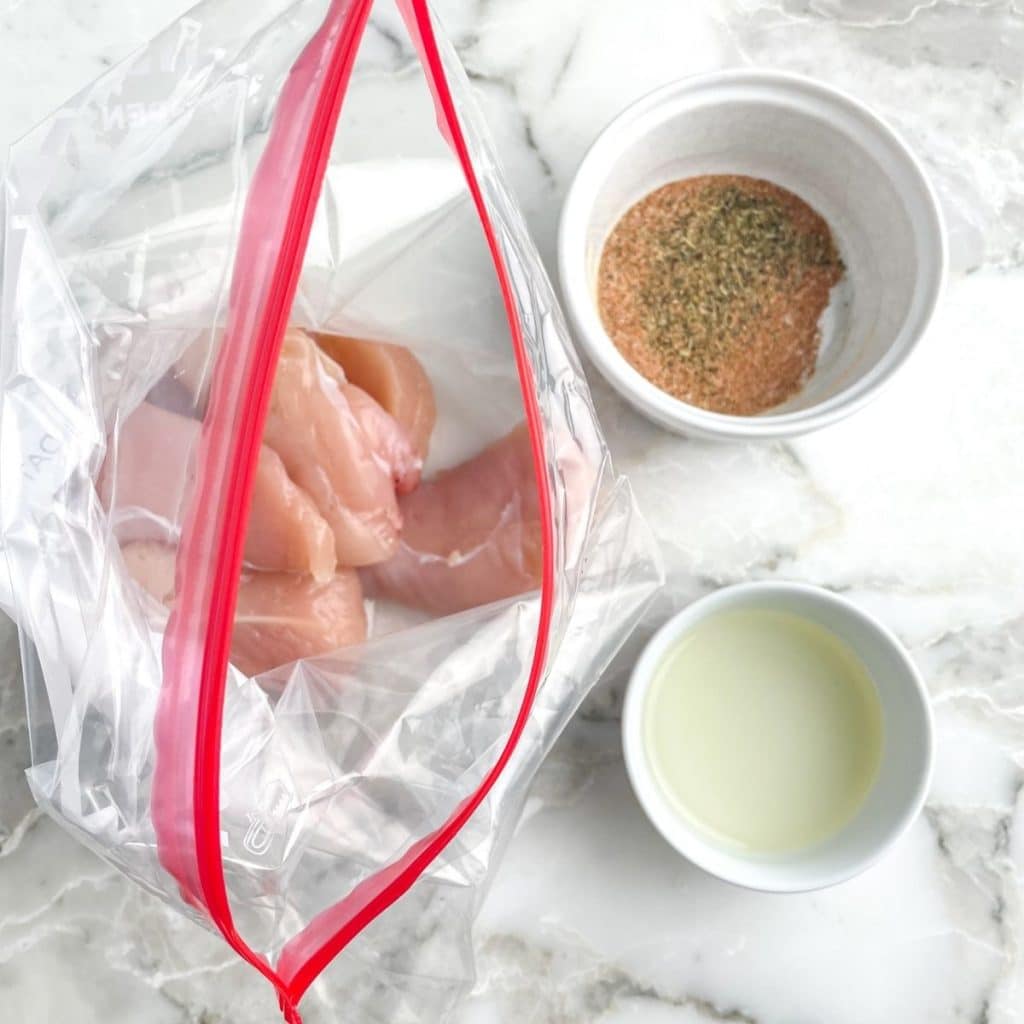 Chicken tenders in a ziploc bag. Spices and oil in small bowls.