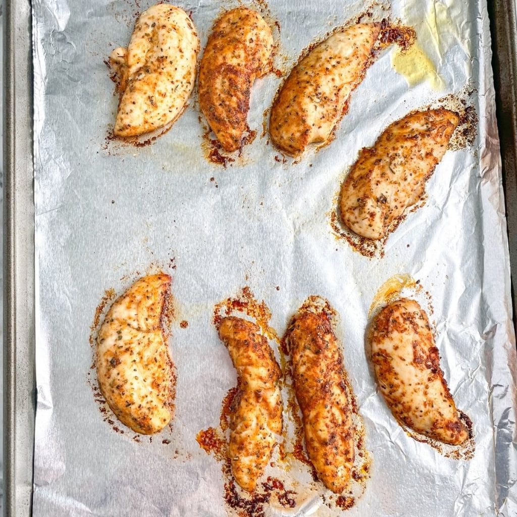 Cooked chicken tenders on foil lined baking sheet.