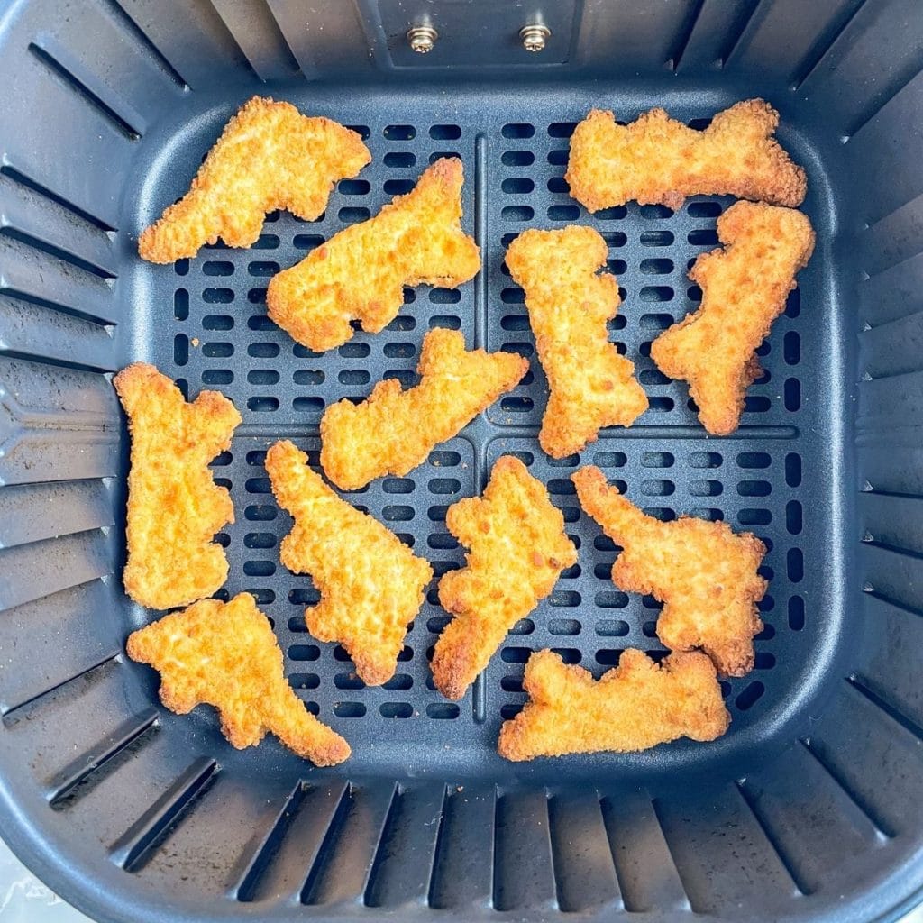 Cooked dino nuggets in air fryer basket.