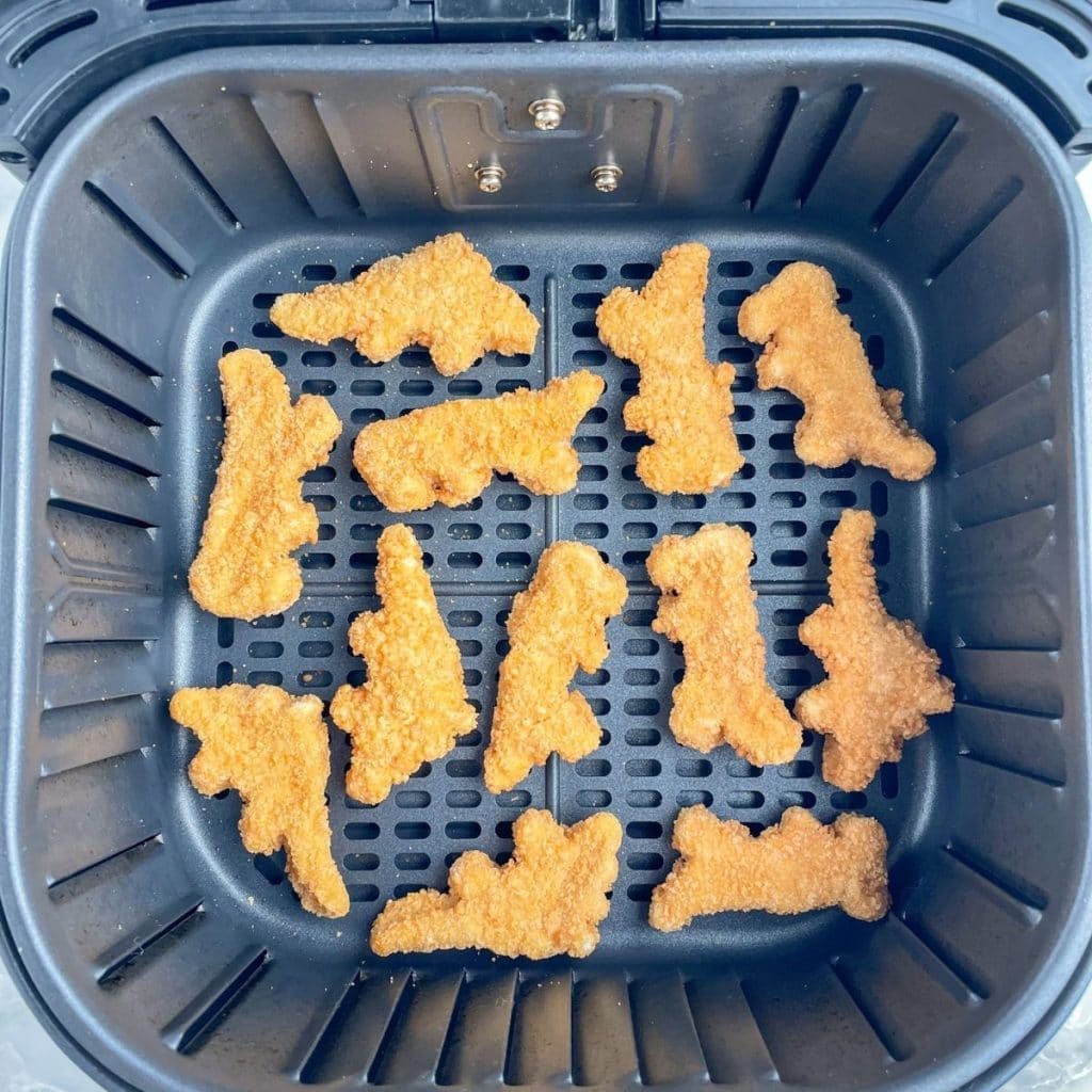 Frozen chicken nuggets in air fryer basket.