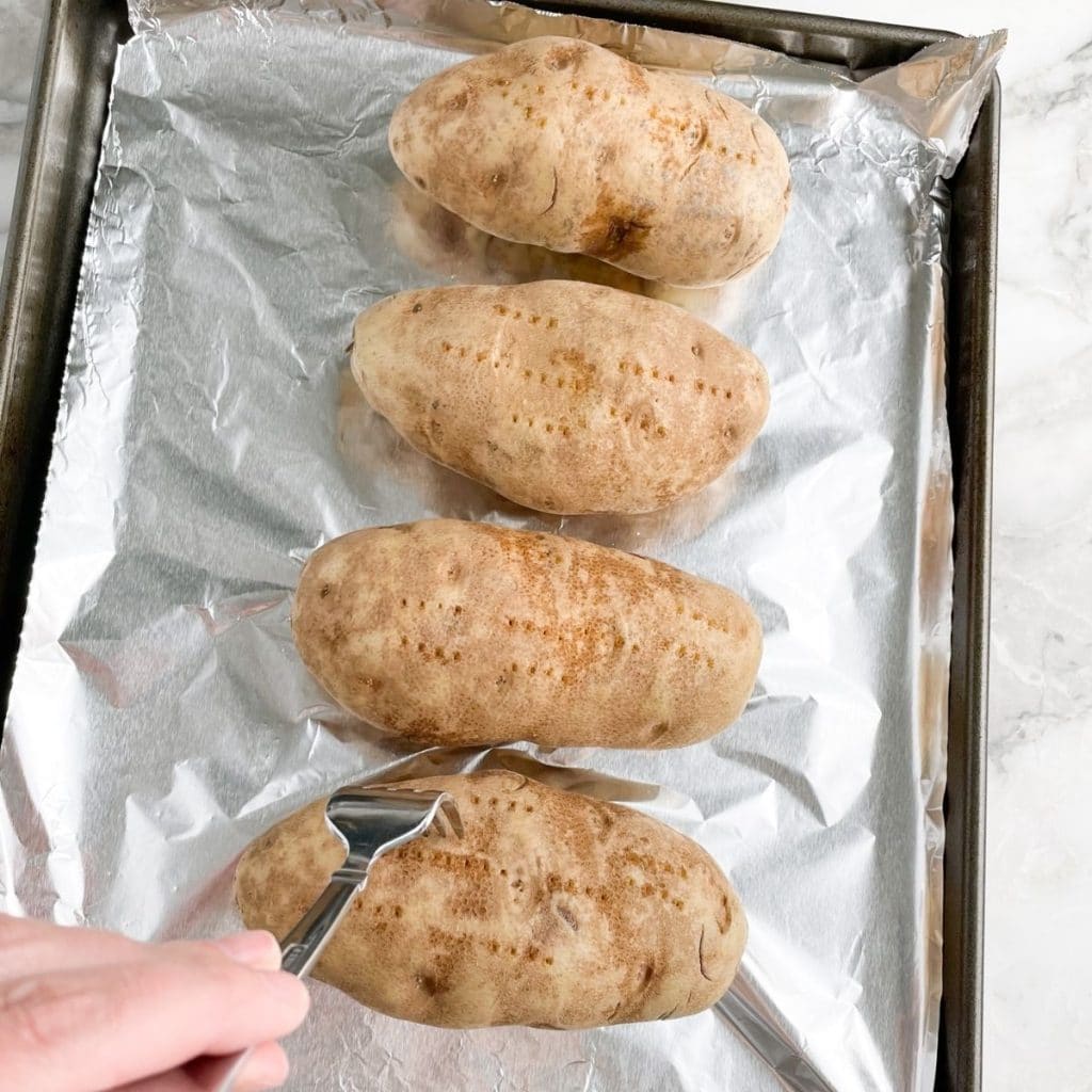 Potatoes on a baking sheet with fork. 