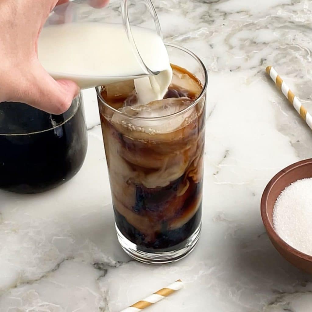 Cream pouring into glass with iced coffee.