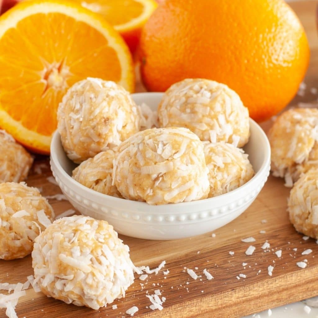 Coconut balls in a bowl and slices of orange.
