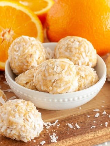 Coconut balls in a bowl and slices of orange.