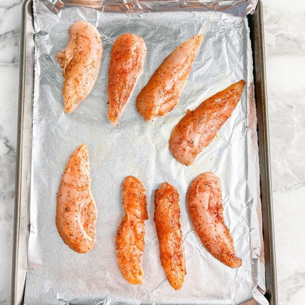 Uncooked chicken tenders on foil lined baking pan.