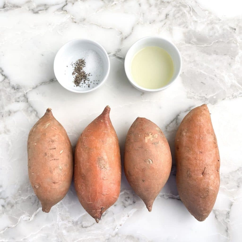 Four sweet potatoes with bowl of oil and salt and pepper. 