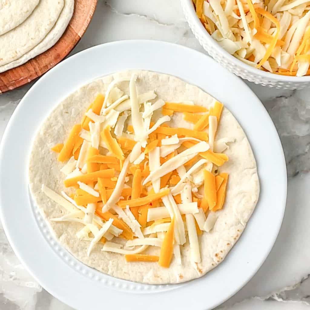 Plate with tortilla topped with shredded cheese.