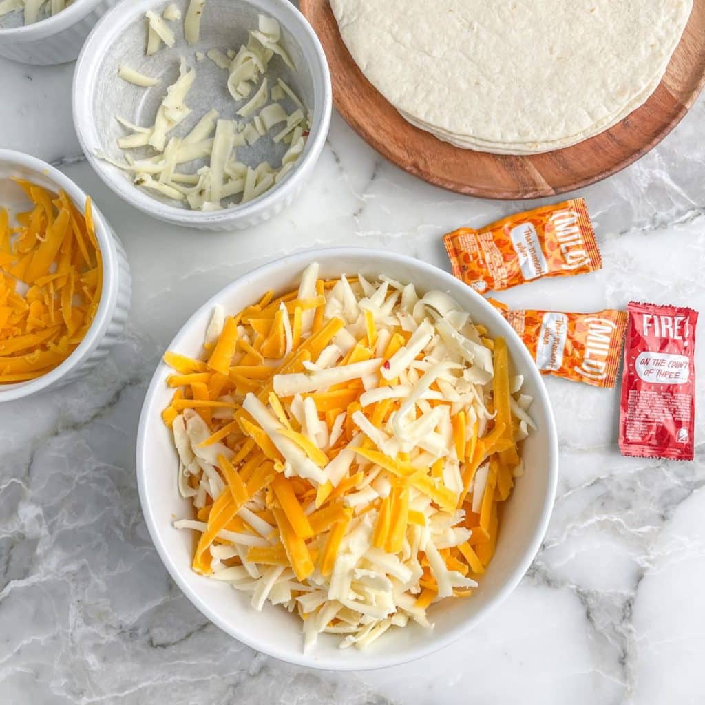 Bowl of shredded cheese and flour tortilla. 
