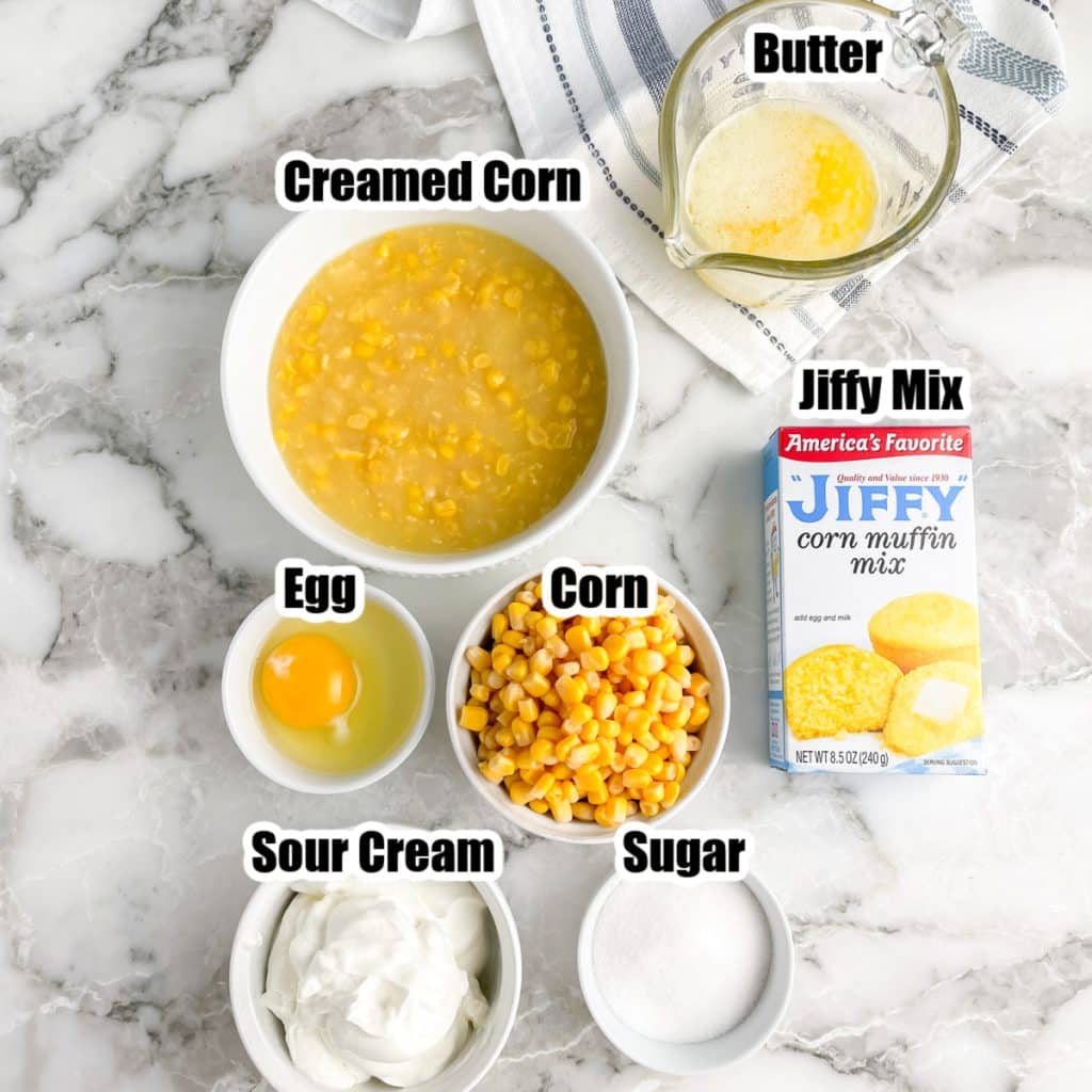 Bowl of corn, butter, egg, sour cream, sugar, and box of Jiffy corn mix.