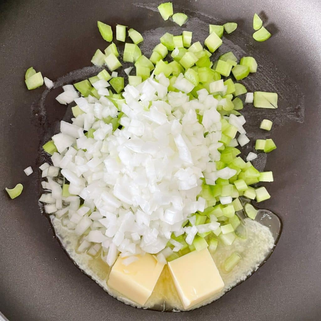 Skillet with butter, diced onion, and celery. 