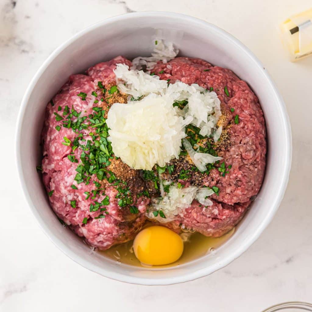 Bowl of ground beef, pork, breadcrumbs, parsley, and egg. 