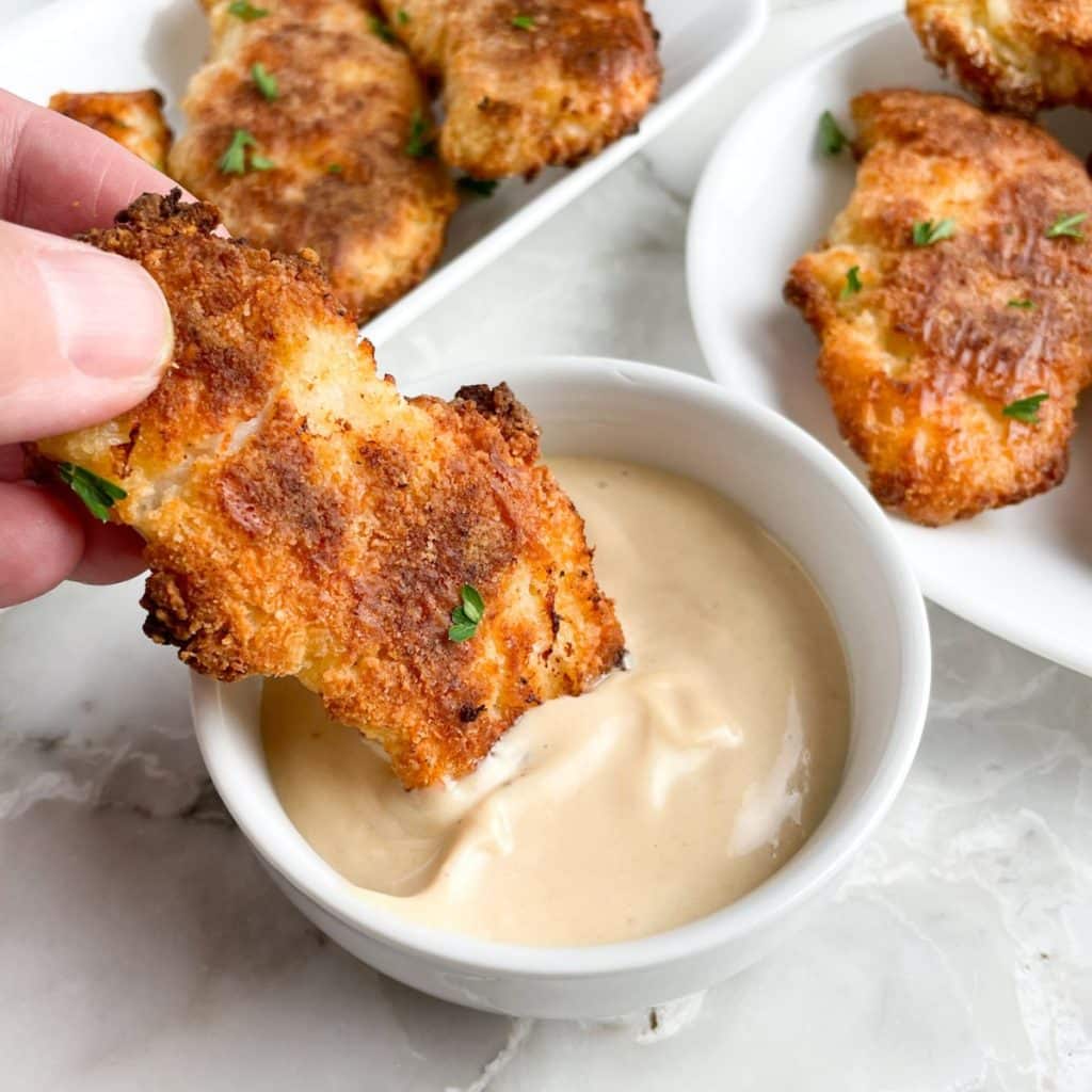 Breaded chicken tenders dipping into sauce.