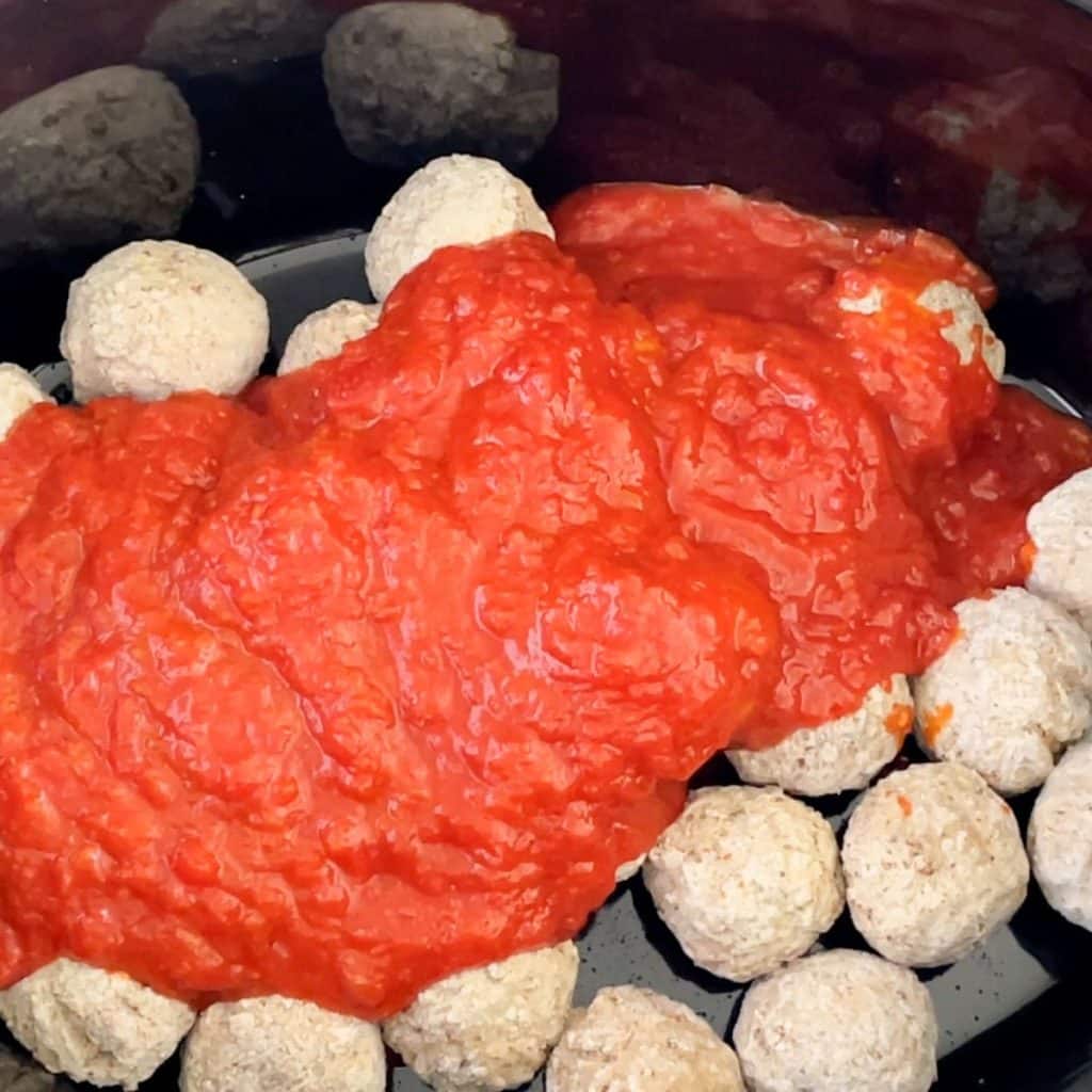 Slow cooker with frozen meatballs and red sauce. 