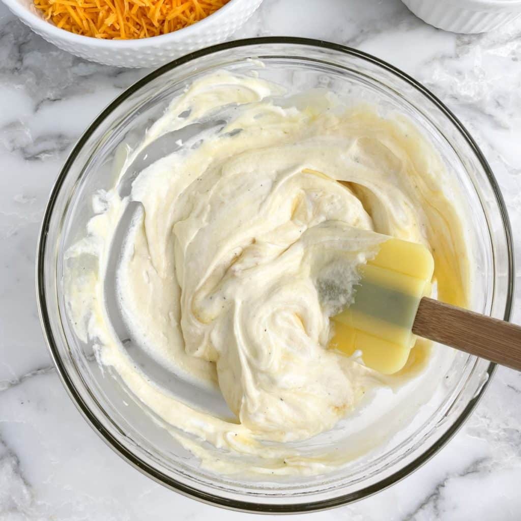 Bowl with creamy sauce and a yellow spatula. 