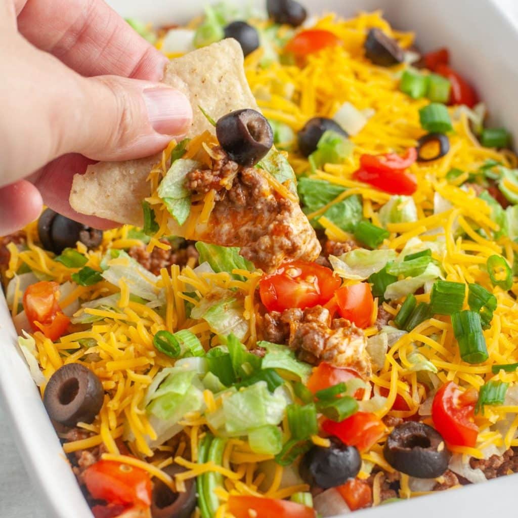 Hand holding tortilla chip with beef taco dip. 