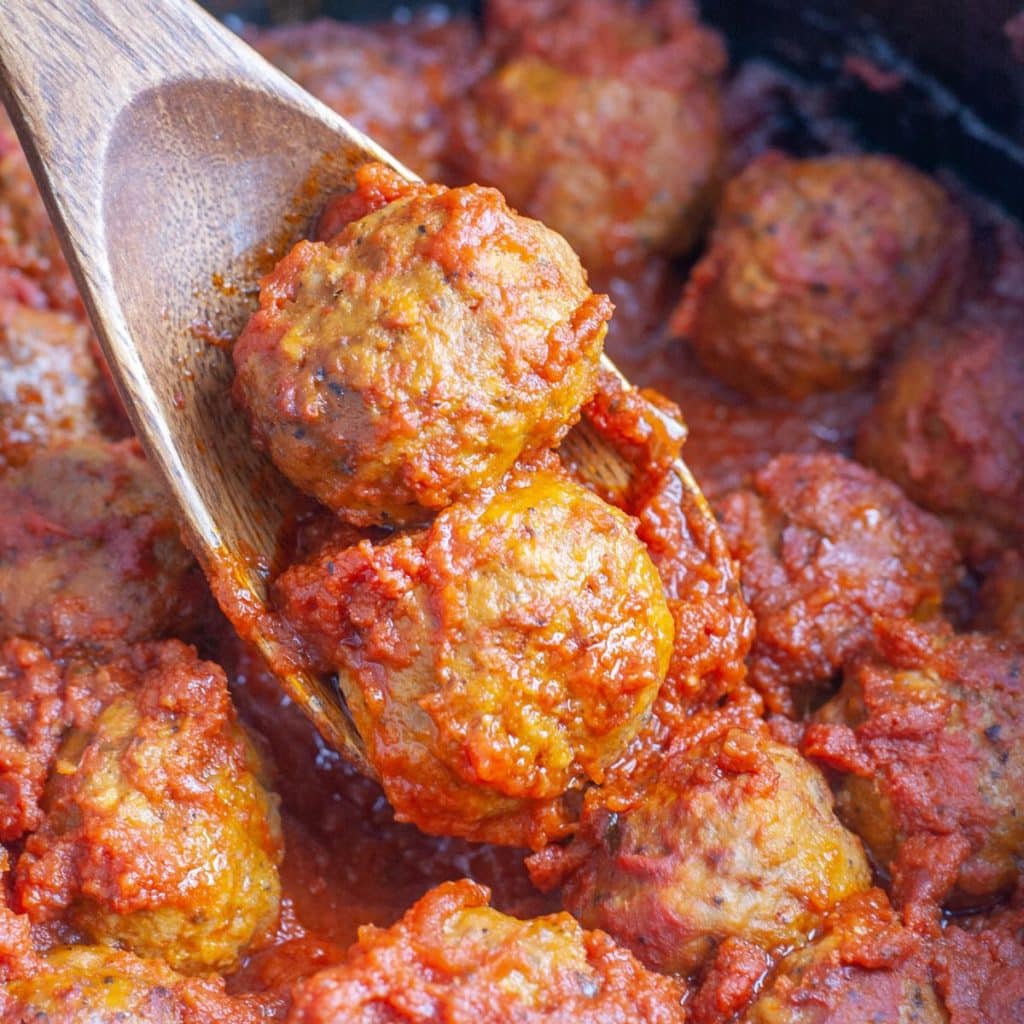 Wooden spoon with meatballs and red sauce.