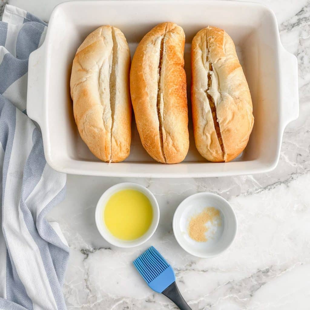 Casserole dish with hoagie rolls, bowl with melted butter and garlic powder.