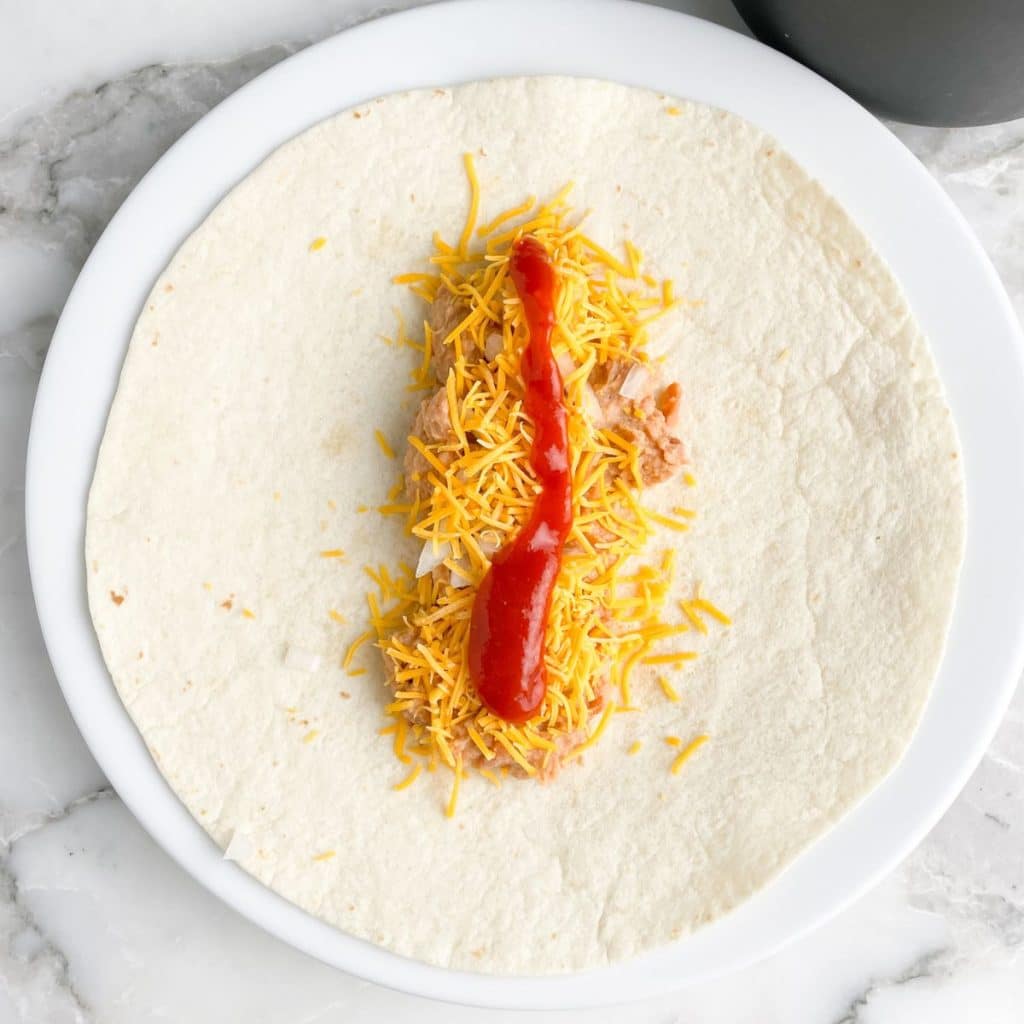 Tortilla with refried beans, onion, shredded cheese, and sauce.