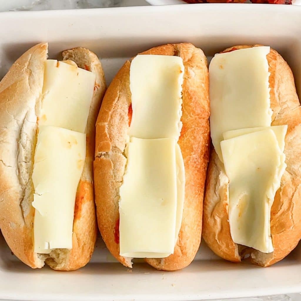 Sandwich rolls in casserole dish topped with mozzarella cheese.