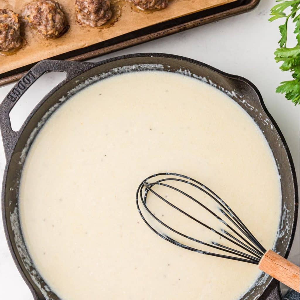 Cream sauce in a pan with a wisk. 
