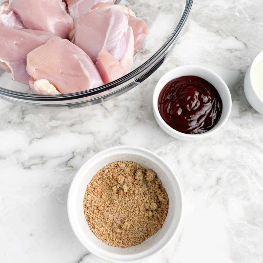 Bowl of chicken thighs, bowl of seasoning, and bbq sauce. 