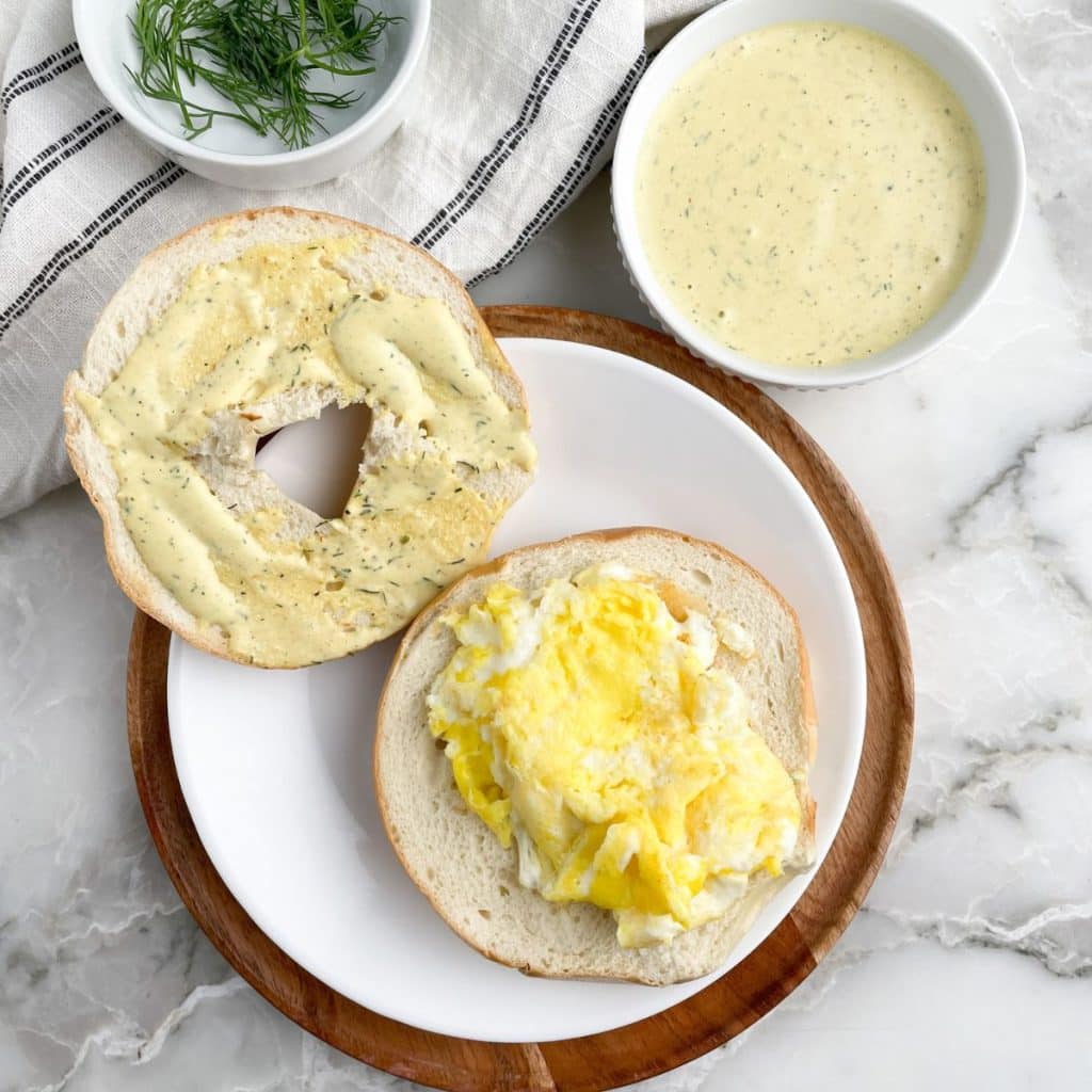 Bagel topped with egg and sauce and a bowl of sauce.