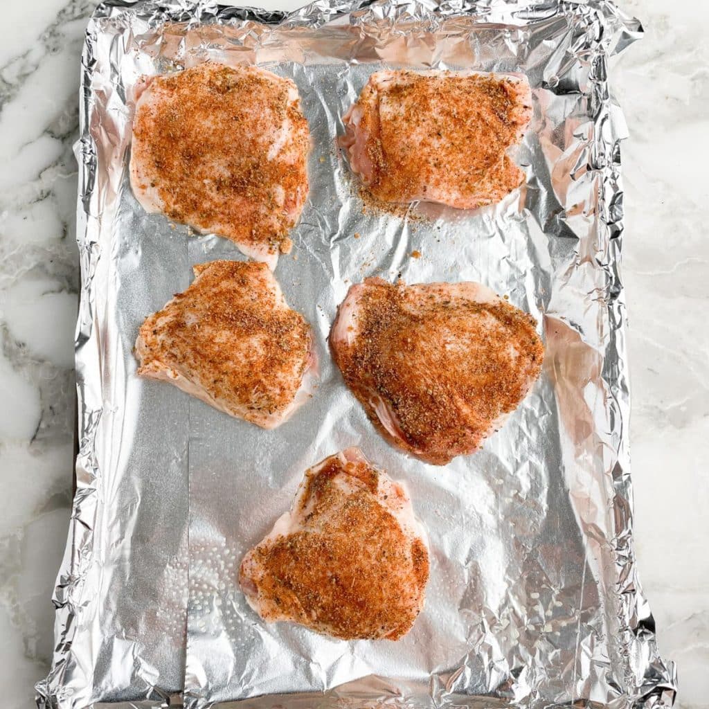 Seasoned chicken thighs on baking sheet. 