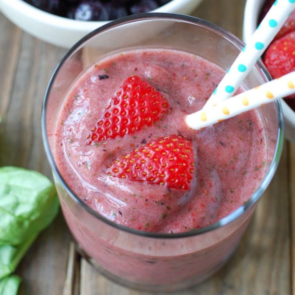 Berry smoothie in glass with cut up strawberries. 