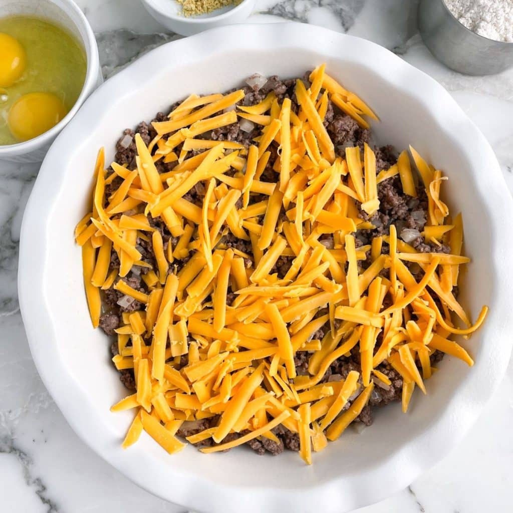 Pie plate with ground beef and shredded cheese. 