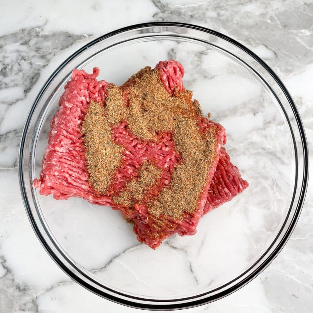 Ground beef with seasonings in a bowl.