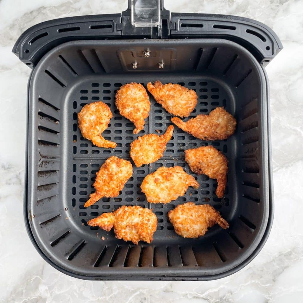 Cooked coconut shrimp in air fryer basket.