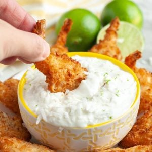 Coconut shrimp dipping in a bowl of creamy sauce.
