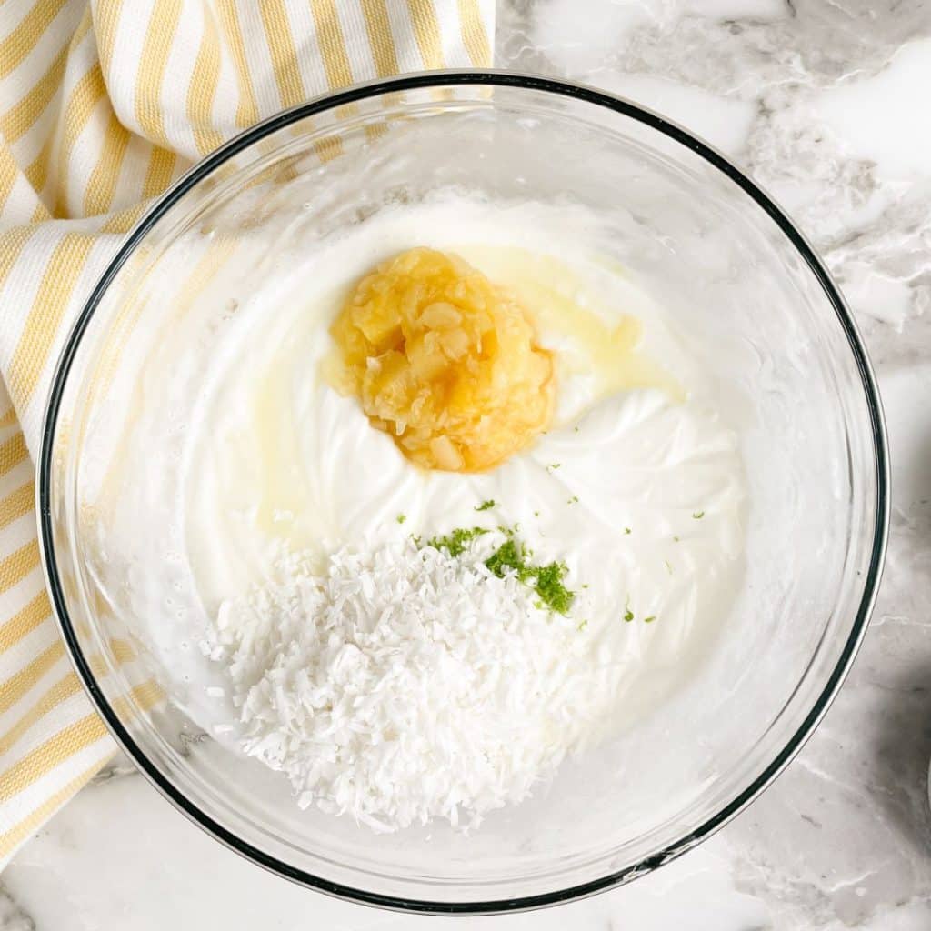 Bowl of creamy sauce with crushed pineapple, shredded coconut, and lime zest.