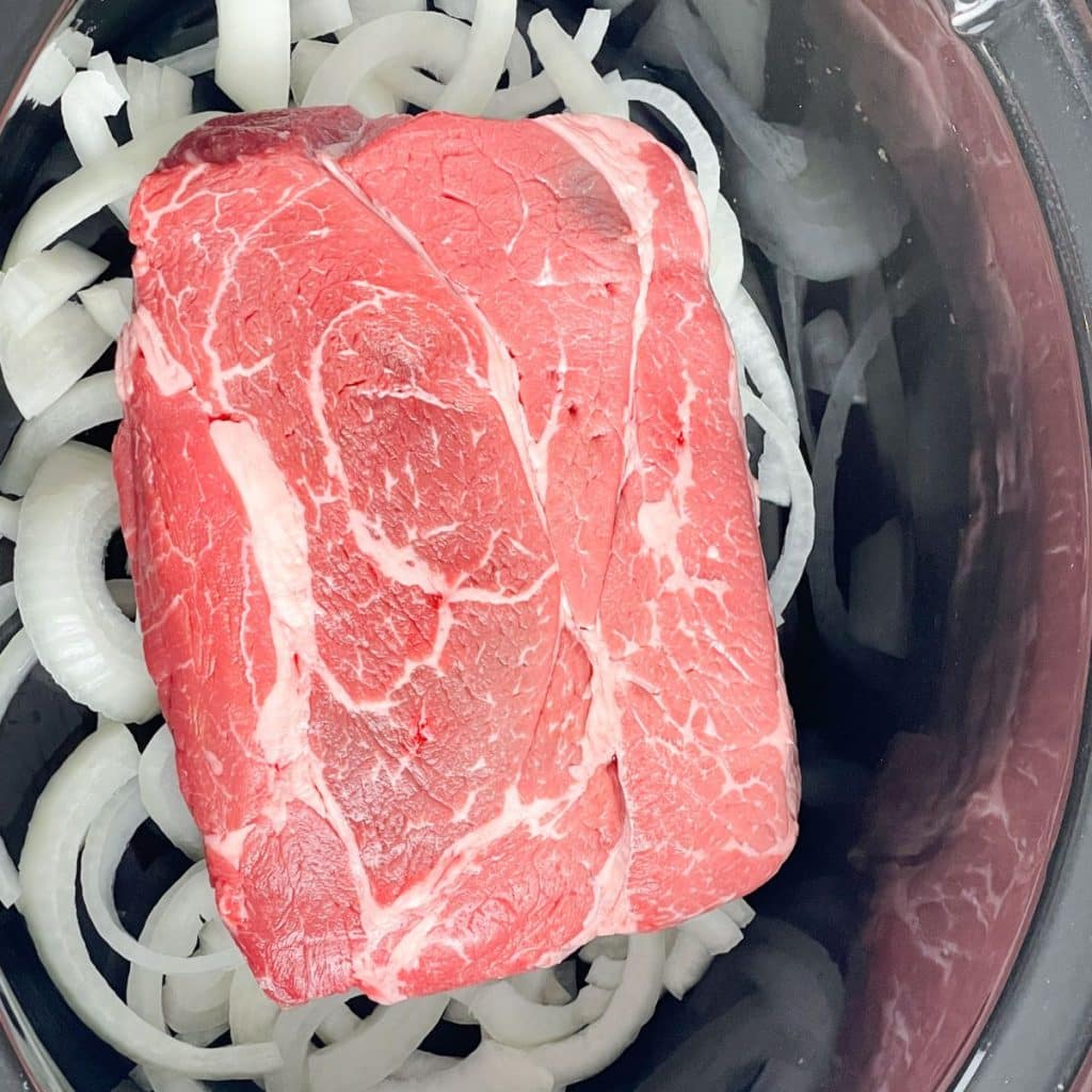 Onions and chuck roast in a slow cooker.